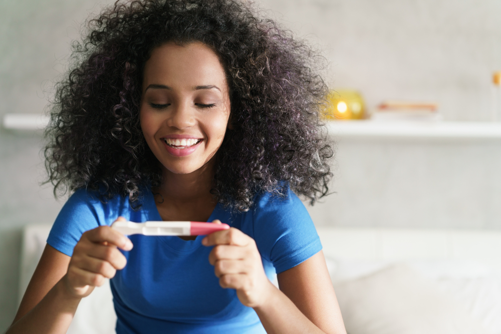 woman looking at pregnancy test result smiling.