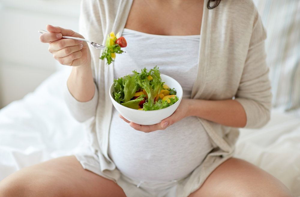 pregnant woman eating vegetable salad for breakfast in bed.