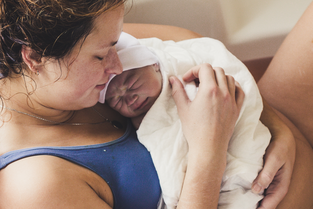 Happy woman in bath holds her amazing newborn baby